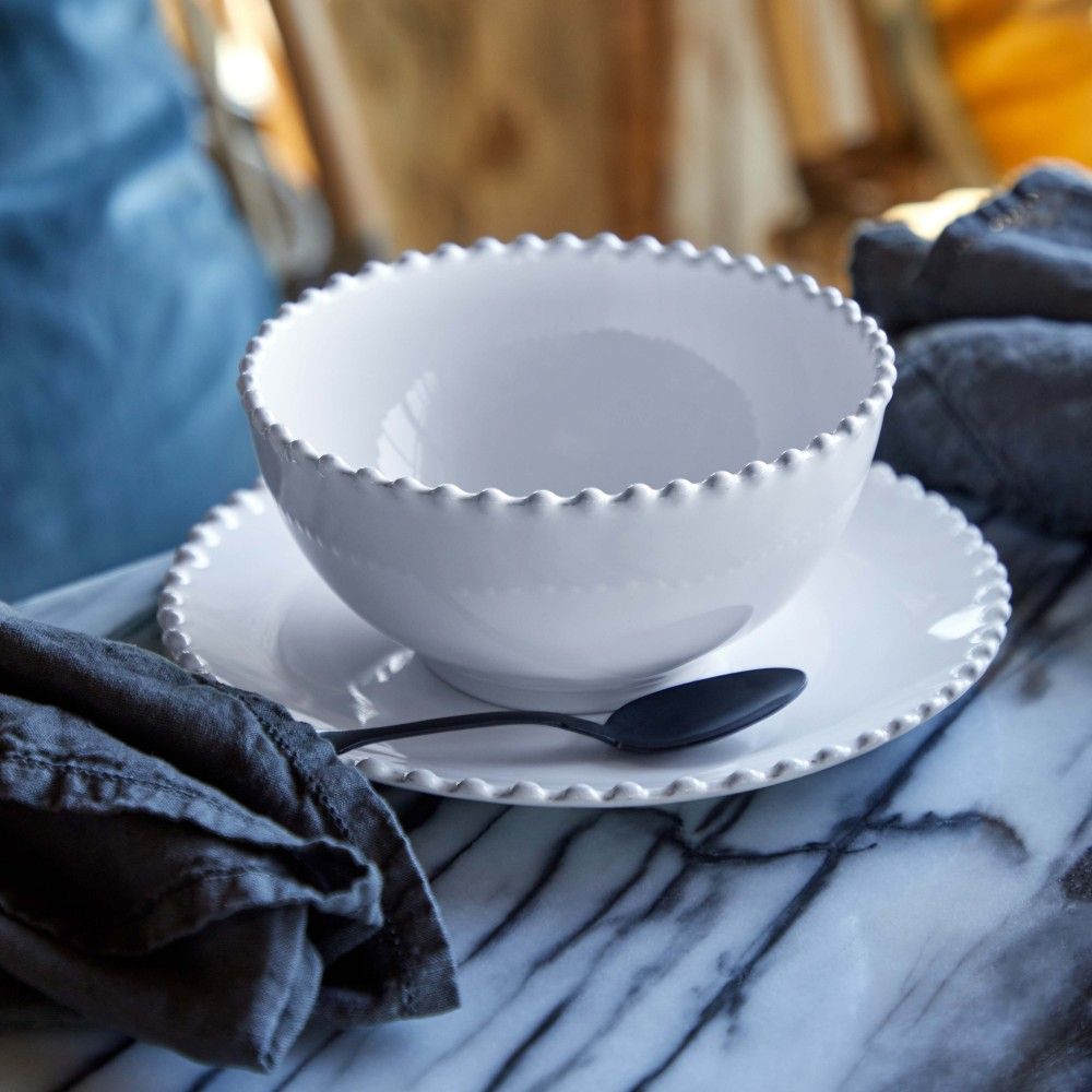bol blanc à soupe et à cereales avec perles sur le rebord posé sur une table marbrée avec des serviettes en lin bleu denim