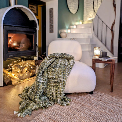 une chauffeuse en tissu bouclette blanc en lin vue de face, et un plaid vert posé invitant à la détente. Maison gabin décoration.