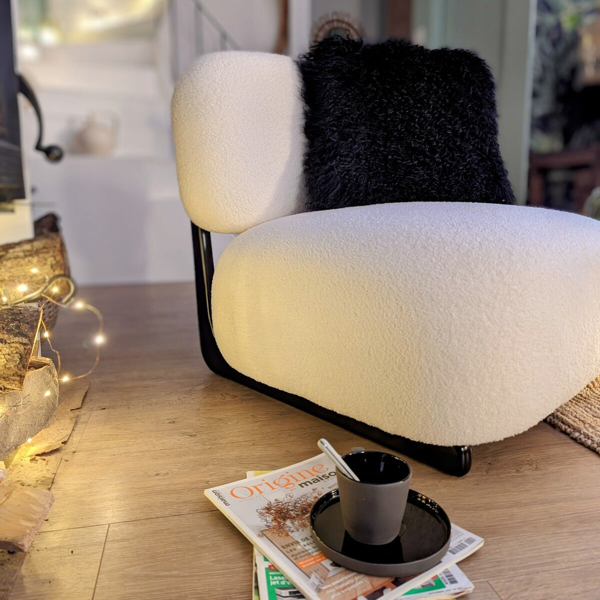 chauffeuse avec un revêtement en lin bouclé et armature en bois foncé accueillant un coussin noir à poils de mouton