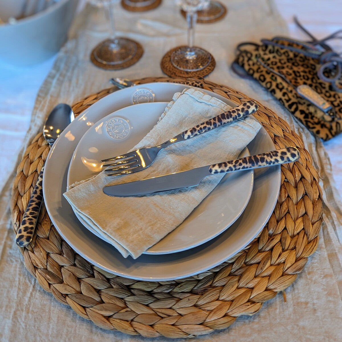 un chemin de table kaki clair accueillant une vaisselle beige en grès fin, une serviette en lin beige et des couverts leopard