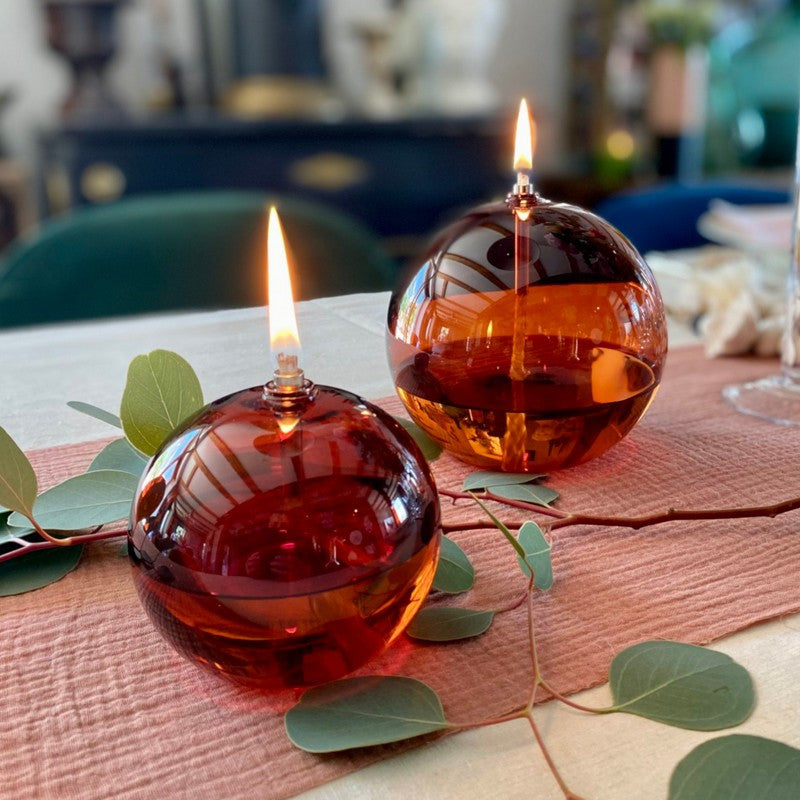 lampe à huile sphère orange en verre transparent allumée grâce à la mêche en coton baignant dans l'huile de paraffine