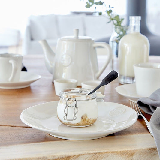 une jolie vaisselle blanche posée sur une table. Assiette, tasses et soucoupes égaient le moment du petit déjeuner. Maison gabin decoration