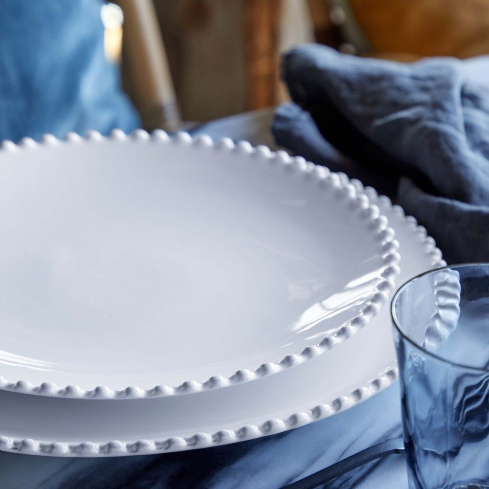 belle assiette à dessert blanche avec des perles et son assiette à dîner de la même collection posées sur une table sublimées par une serviette en lin bleu. Maison gabin decoration