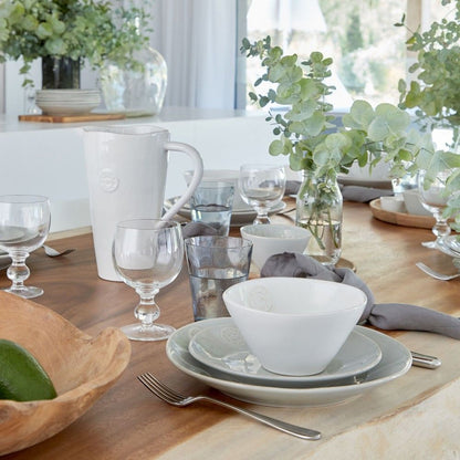 une table dressée avec une vaisselle de couleurs mélangées. bol blanc, assiette à dessert et à diner beiges, complétés de verres et d'une carafe. Maison-gabin-décoration