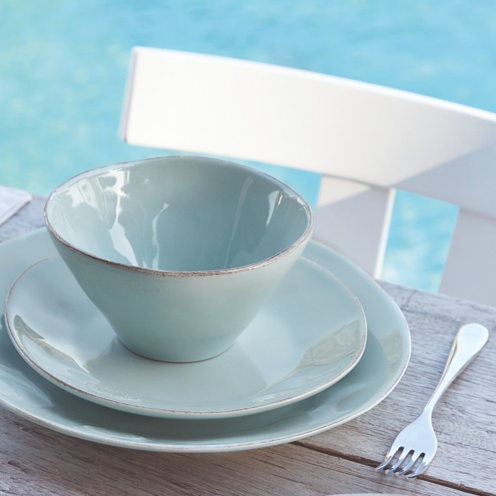 un bol, une assiette à dessert et une assiette à diner de couleur turquoise sont posés sur une table au bord de la piscine créant une ambiance estivale, un moment de vacances- Maison gabin décoration