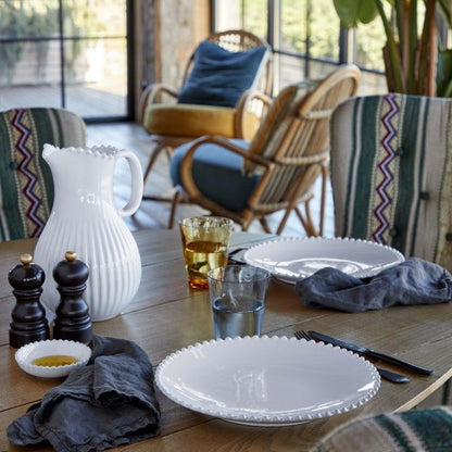 une assiette blanche à perles sur le bord de l'assiette, en grès fin, est posée sur une table avec une belle carafe à eau blanche. Maison gabin decoration