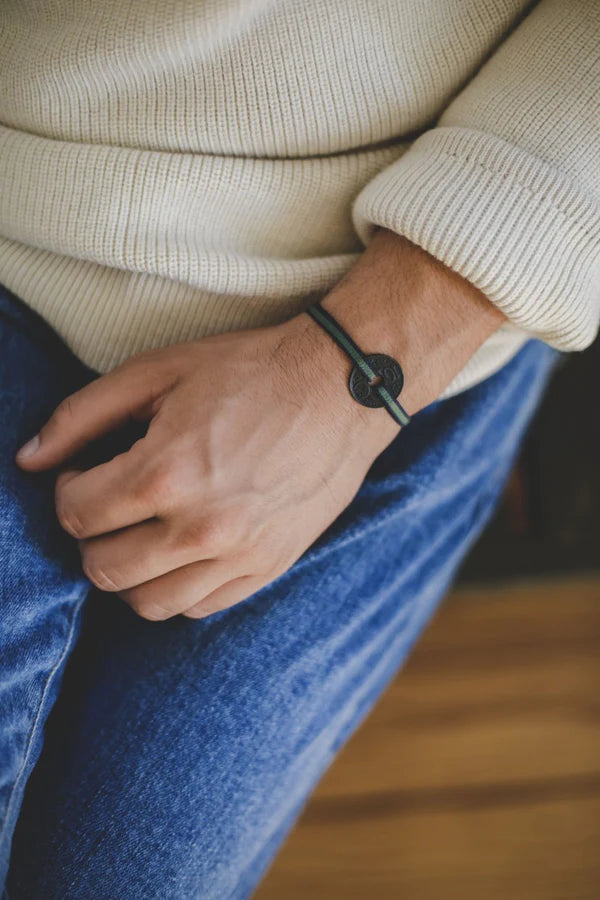 un bracelet fait avec le sou français, teinté en noir. Troué au centre passe un cordon élastique réglable vert avec un liseret noir. Maison Gabin décoration