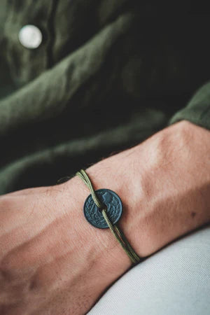 un bracelet composé d'une pièce de 10cts trouée teintée couleur charbon avec un cordon kaki. Maison gabin décoration