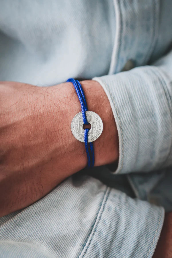 un bracelet avec une pièce de monnaie française trouée par lequel passe un cordon réglable bleu foncé. maison gabin décoration