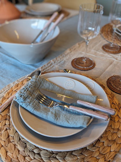 une serviette de table 100% lin beu mint posée dans une assiette à dessert beige avec des couverts imprimé pierre. Maison gabin décoration